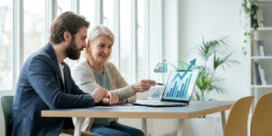 Un conseiller financier montre un graphique boursier en hausse sur un ordinateur portable à une cliente senior.